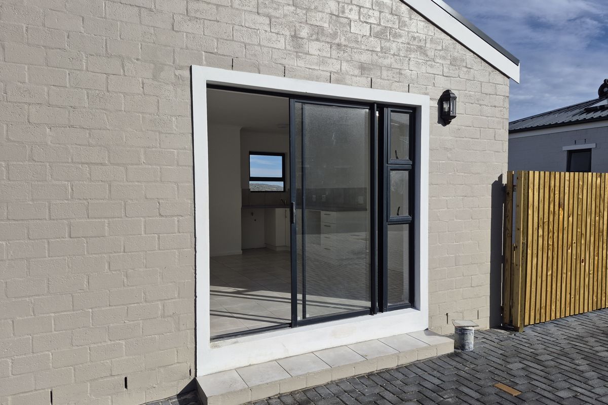 Rear exterior view of the apartment featuring a sliding glass door, brick facade, and paved patio area with timber fencing.