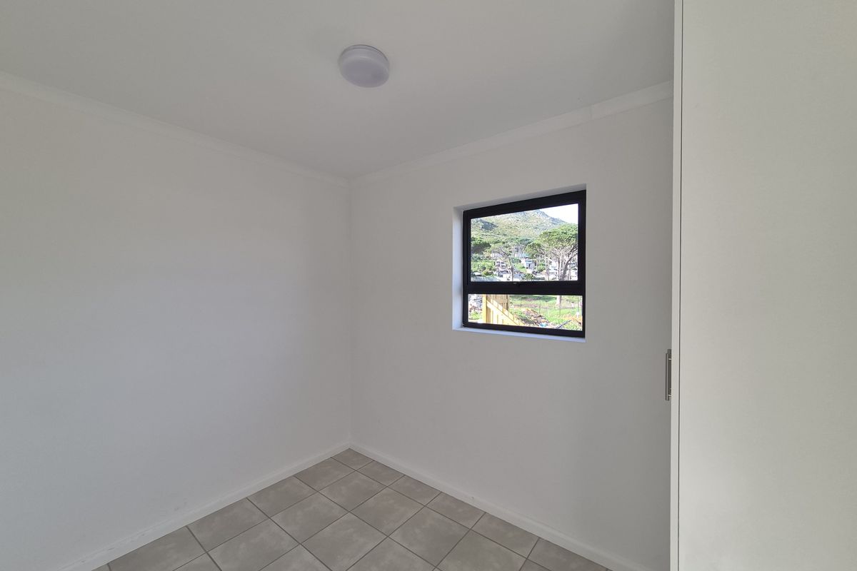 A clean, empty bedroom featuring neutral tiled flooring, white walls, and a built-in cupboard with a view through the window.