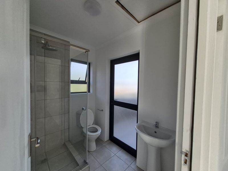 A clean, modern bathroom featuring a glass-enclosed shower, pedestal basin, and toilet, with tiled flooring and a frosted glass door for privacy.