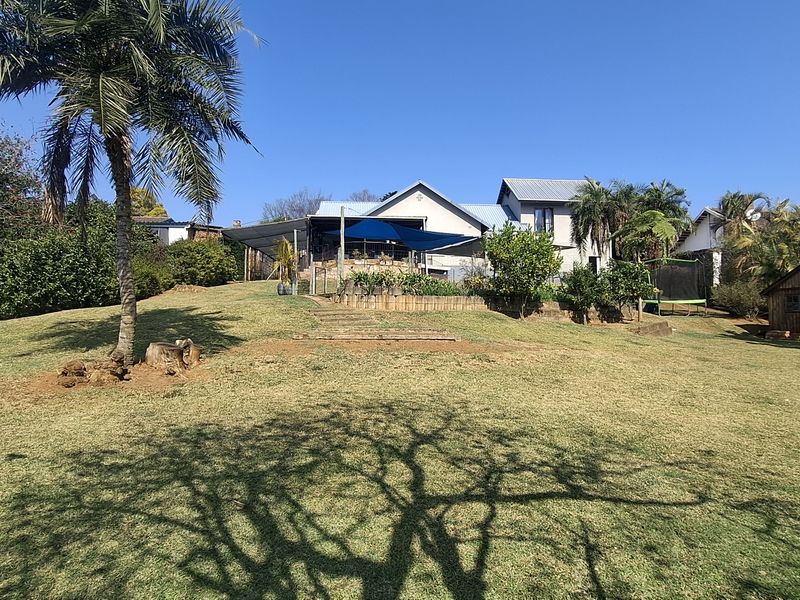Spacious rear garden featuring a large lawn, mature trees, a timber storage shed, and a covered patio area attached to the main residence.