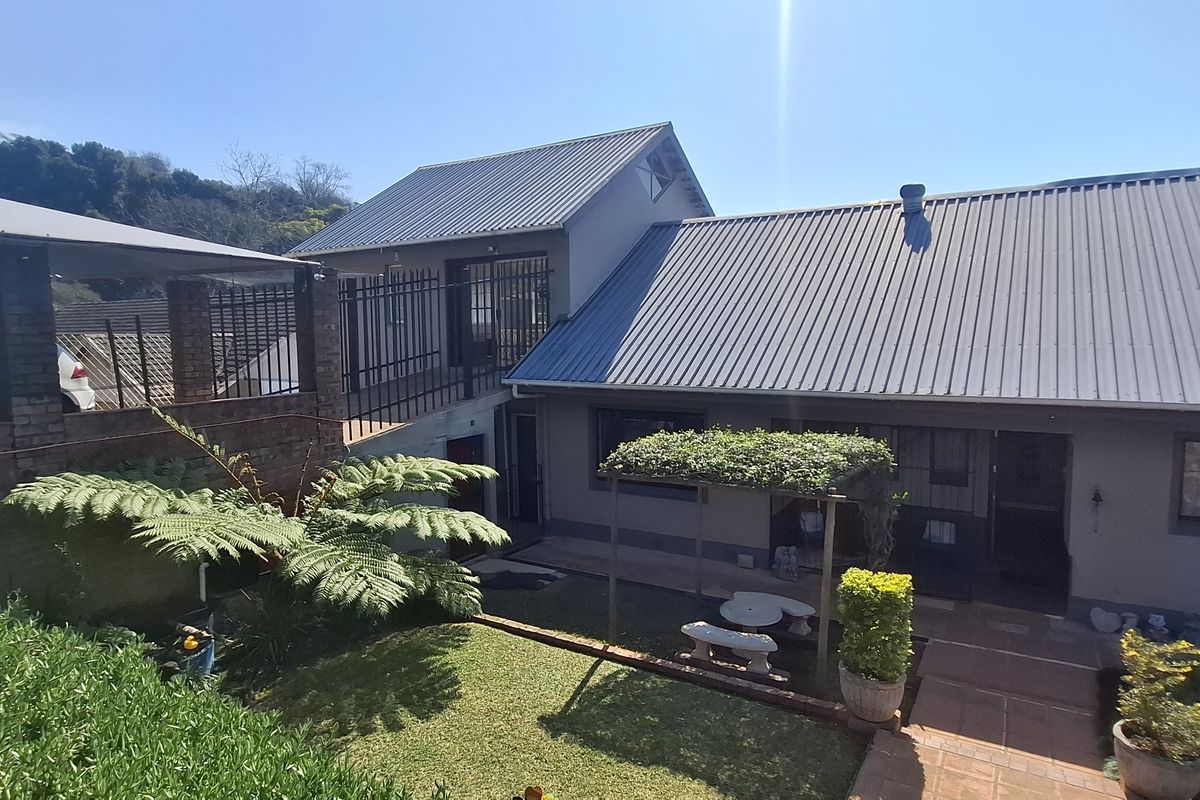 Rear view of the property featuring a corrugated metal roof, paved patio area, pergola, and a raised walkway with security fencing.