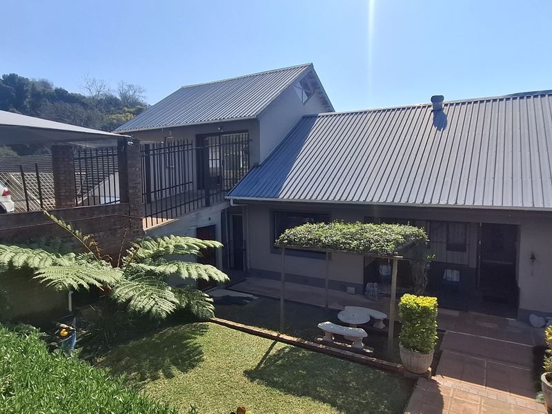 Rear view of the property featuring a corrugated metal roof, paved patio area, pergola, and a raised walkway with security fencing.