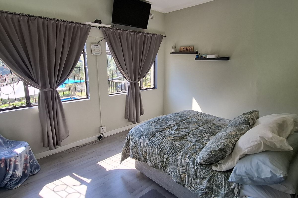 A functional bedroom featuring laminate flooring, security bars on windows, and wall-mounted floating shelves.