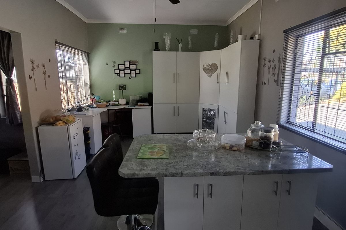 A functional kitchen area featuring white built-in cabinetry, a central island with a stone-look countertop, and large windows with venetian blinds.