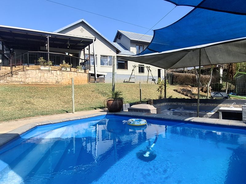 Outdoor pool area featuring a swimming pool, shade sails, and a raised covered patio with stone retaining wall.
