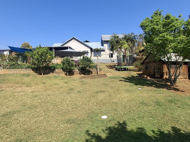 Spacious rear garden featuring a lawn, established trees, a timber storage shed, and a raised patio area attached to the main house.