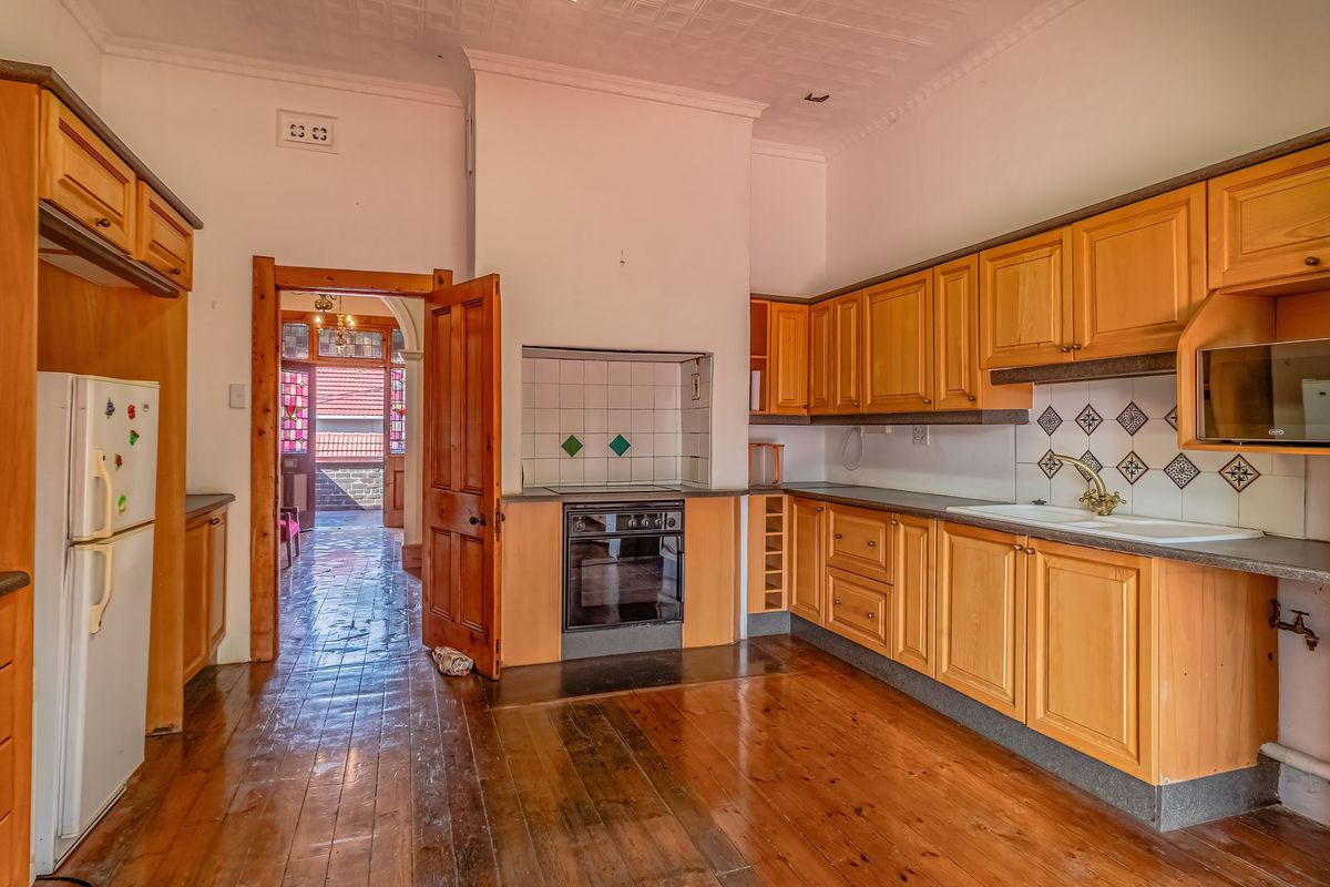 A spacious kitchen featuring timber cabinetry, built-in oven, tiled splashback, and original timber flooring, offering a classic layout with potential for modern updates.