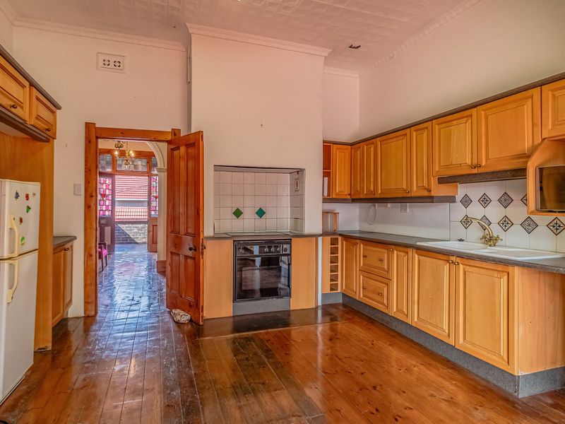 A spacious kitchen featuring timber cabinetry, built-in oven, tiled splashback, and original timber flooring, offering a classic layout with potential for modern updates.