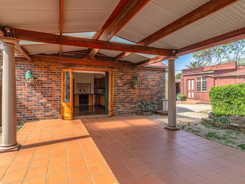 A covered outdoor patio featuring tiled flooring, exposed timber beams, and a corrugated metal roof, providing direct access to the interior living space.