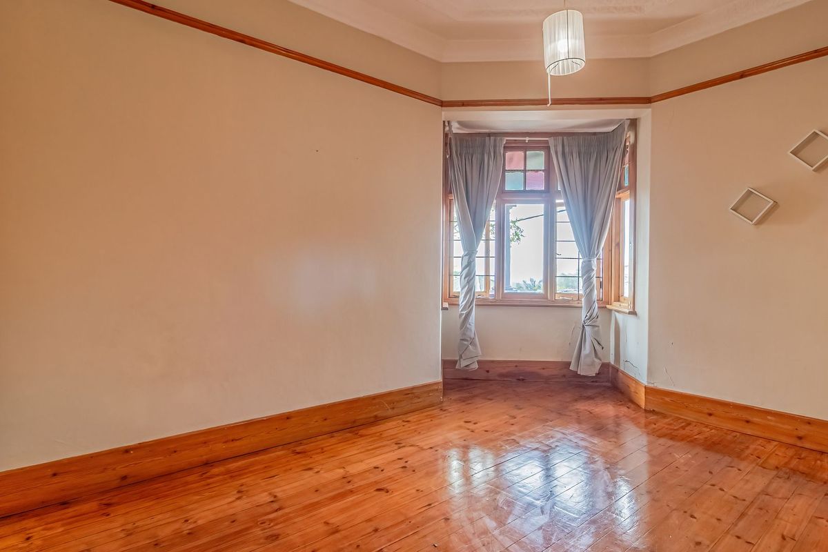 An empty bedroom featuring polished timber flooring, timber window frames, and classic picture rails, requiring some minor plaster and paint repairs.