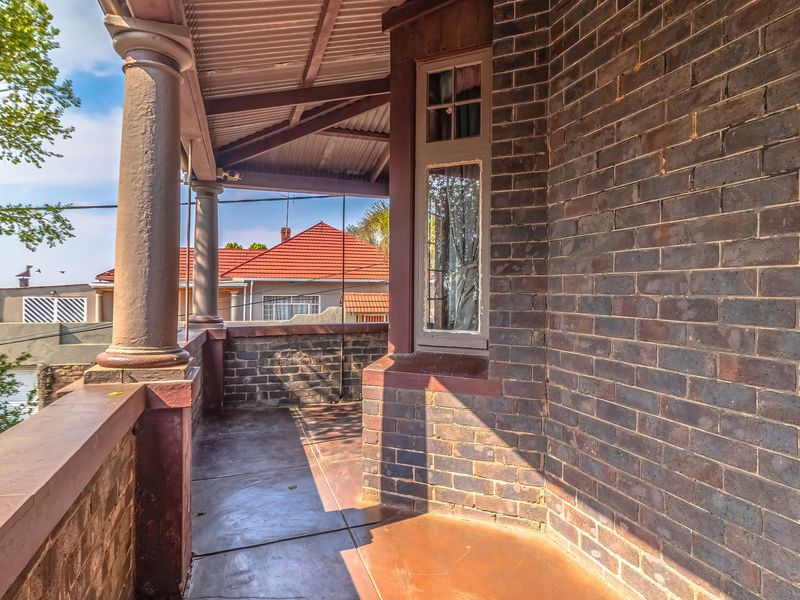 A covered brick veranda featuring classic architectural columns and concrete flooring, offering a traditional outdoor space.