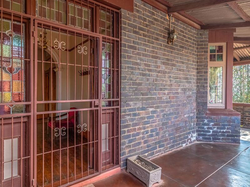 A covered front patio featuring exposed brick walls, a leaded glass entrance door with security screen, and a timber-lined ceiling.