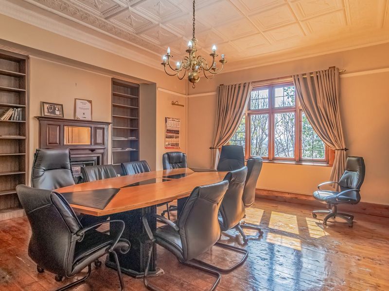 Spacious home office featuring original timber flooring, decorative ceiling detail, built-in shelving, and a classic fireplace mantel with leaded glass windows.