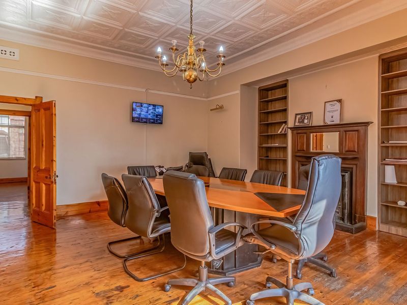 A formal office or boardroom featuring a classic pressed metal ceiling, polished timber flooring, and built-in shelving with a traditional fireplace mantel.