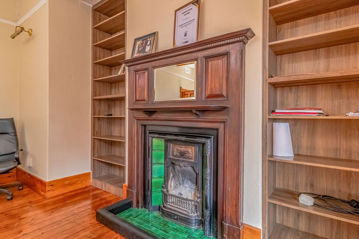 A cozy living area featuring a classic fireplace with a wooden mantel, green tiled hearth, and extensive built-in wooden shelving on either side.