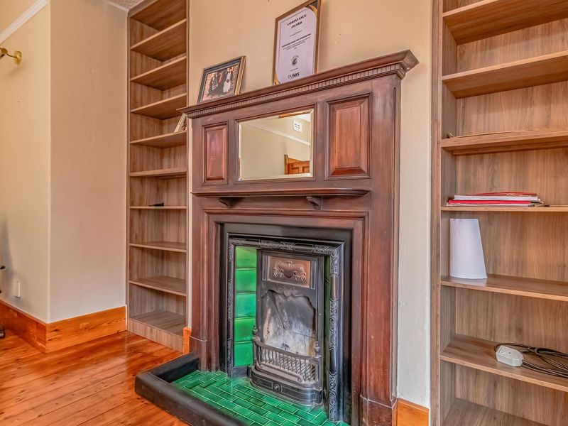A cozy living area featuring a classic fireplace with a wooden mantel, green tiled hearth, and extensive built-in wooden shelving on either side.
