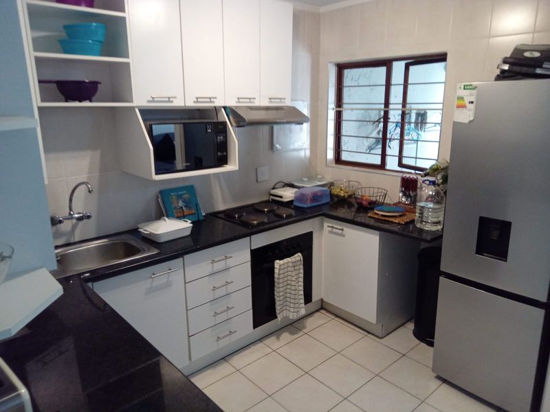 A functional kitchen featuring white cabinetry, black granite countertops, built-in oven and hob, tiled backsplash, and tiled flooring.
