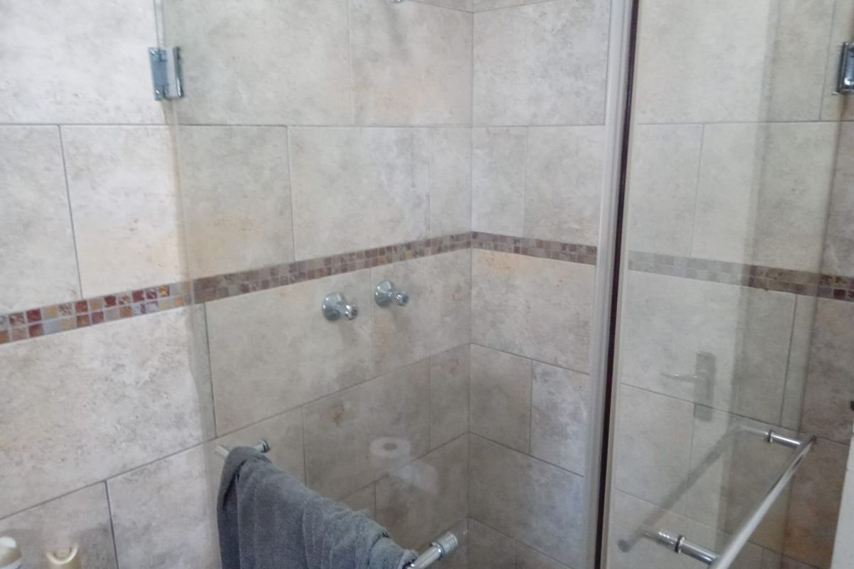 A clean bathroom shower area featuring neutral stone-look wall tiles with a decorative mosaic accent strip and a glass enclosure.