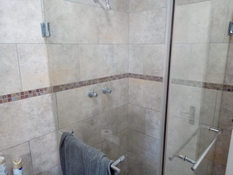 A clean bathroom shower area featuring neutral stone-look wall tiles with a decorative mosaic accent strip and a glass enclosure.