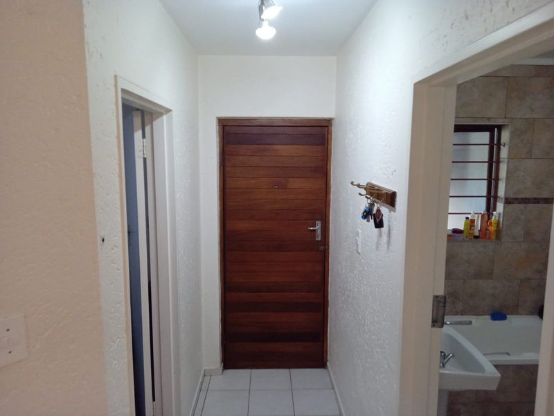 A functional apartment entryway featuring a solid timber front door, neutral ceramic floor tiles, and direct access to adjacent rooms.