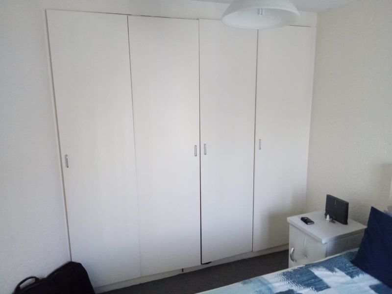 A bedroom featuring a large, white built-in wardrobe with four doors, providing ample storage space.