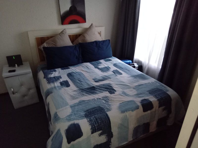 A compact bedroom featuring a window with curtains and neutral wall finishes.