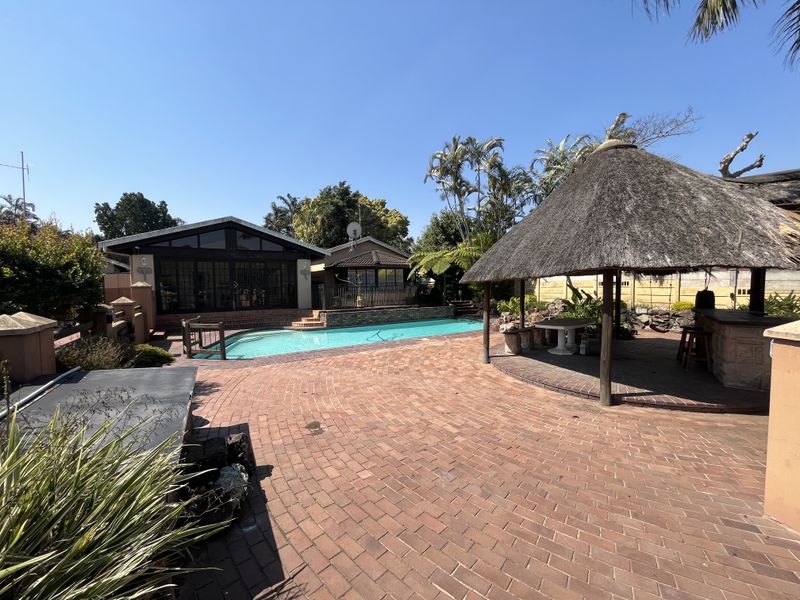 Outdoor entertainment area featuring a swimming pool, brick-paved patio, and a traditional thatched lapa with a built-in bar.
