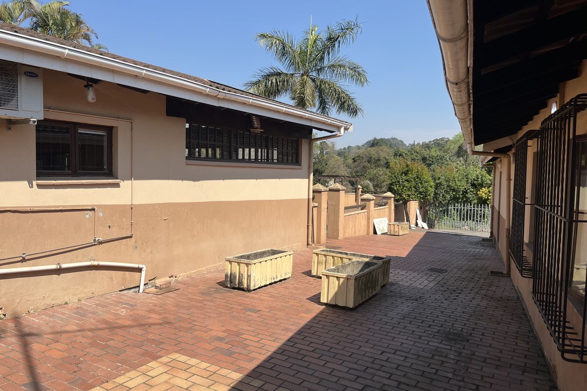 A paved rear courtyard area featuring brick flooring, exterior wall-mounted air conditioning unit, and security bars on the windows.