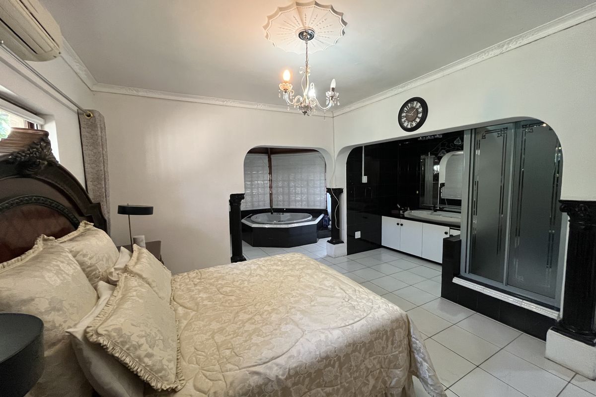 Spacious bedroom featuring an integrated en-suite bathroom with a corner spa bath, shower enclosure, and built-in vanity, complemented by decorative ceiling details.