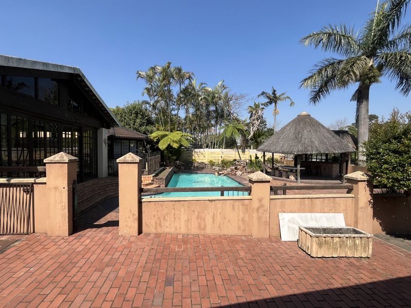 Outdoor pool area featuring a swimming pool, brick paved patio, and a traditional thatched lapa, set within a private garden environment.