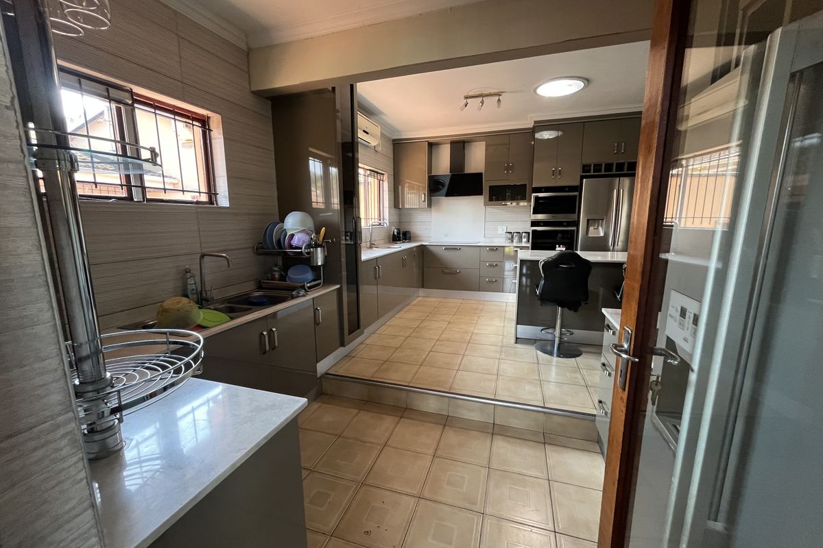 A spacious, modern kitchen featuring high-gloss cabinetry, stone countertops, integrated appliances, and a split-level tiled floor layout.