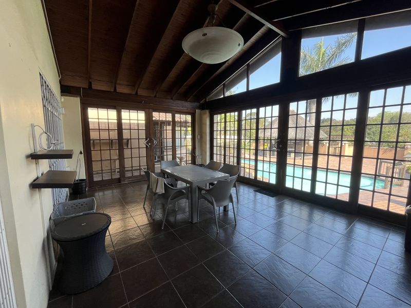 Spacious covered patio featuring exposed timber beam ceilings, dark tiled flooring, and expansive glass doors overlooking the swimming pool area.
