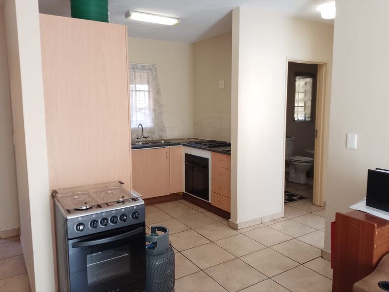 A functional kitchen area featuring light wood-finish cabinetry, a built-in oven with gas hob, tiled flooring, and direct access to an adjacent bathroom.