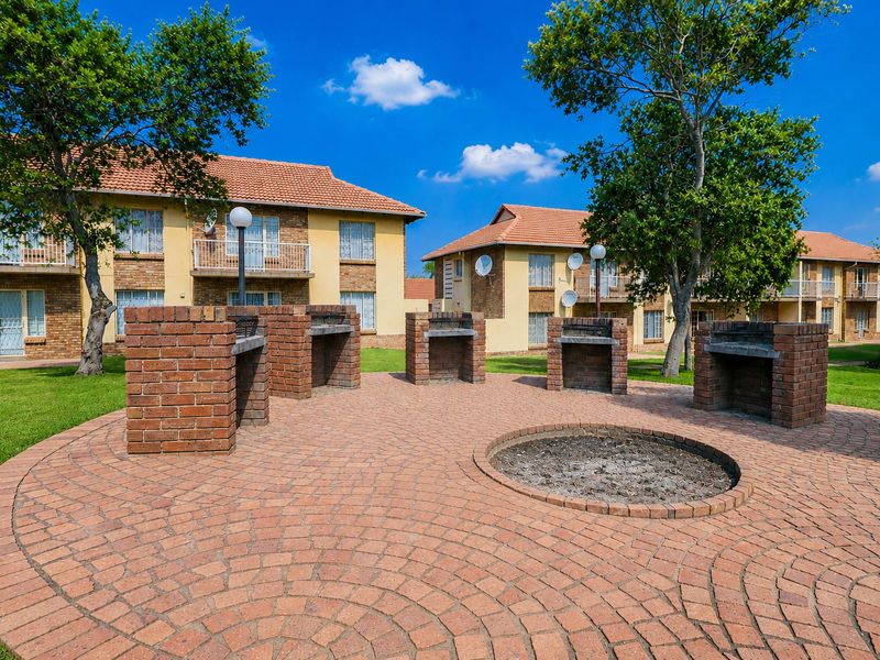 Communal outdoor area featuring multiple brick braai stands and a central fire pit set within a well-maintained apartment complex garden.