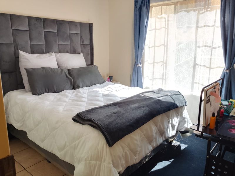 A well-lit bedroom featuring tiled flooring and a large window with natural light, providing a comfortable and functional living space.