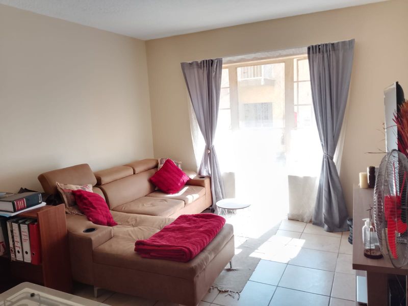 A bright living room featuring tiled flooring and a large window with curtains, providing natural light to the space.