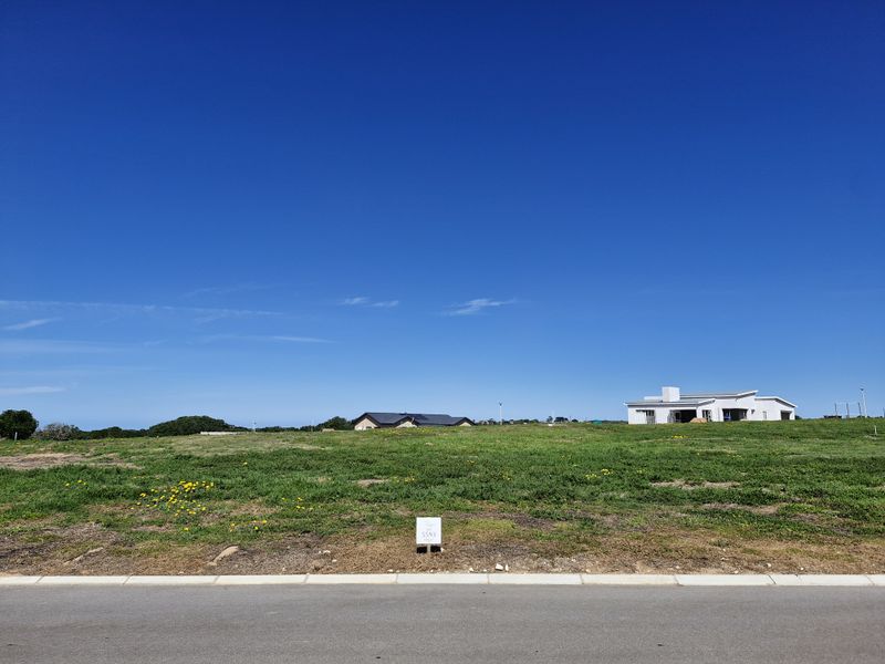 A clear, elevated view of a vacant residential plot featuring established grass cover, bordering a paved road with a property marker.