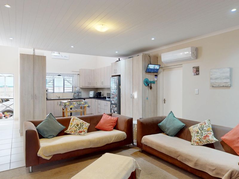Open-plan living and kitchen area featuring light wood-toned cabinetry, tiled flooring, and recessed ceiling lighting with an integrated air conditioning unit.