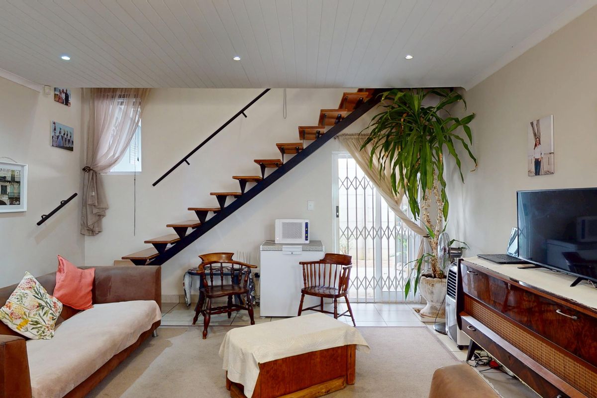 A living room featuring an open-tread staircase, recessed ceiling lighting, and direct access to an outdoor area through a security gate.