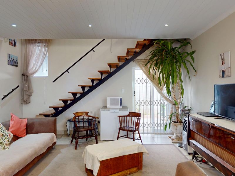 A living room featuring an open-tread staircase, recessed ceiling lighting, and direct access to an outdoor area through a security gate.