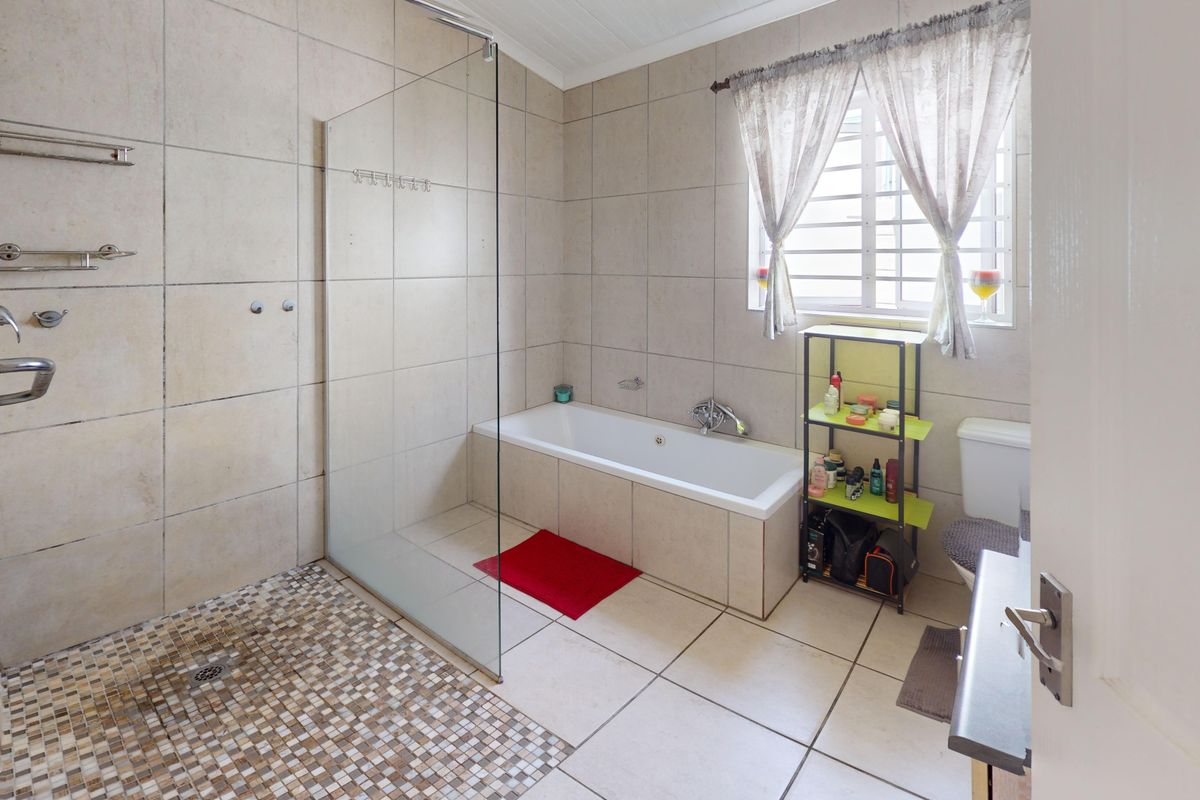 A well-maintained bathroom featuring a walk-in shower with mosaic floor tiles, a built-in bathtub, and neutral wall tiling throughout.