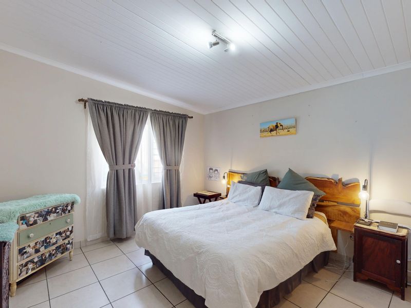 A well-lit bedroom featuring tiled flooring, a white tongue and groove ceiling, and built-in storage cupboards.