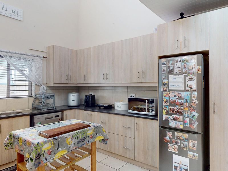 A functional kitchen featuring light wood-look laminate cabinetry, dark countertops, tiled backsplash, and a vaulted ceiling, providing a bright and practical workspace.