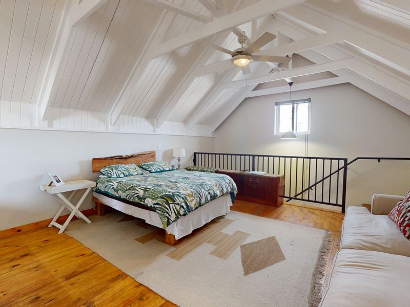 Spacious loft-style bedroom featuring vaulted ceilings with exposed timber beams, polished timber flooring, and a secure metal balustrade overlooking the lower level.