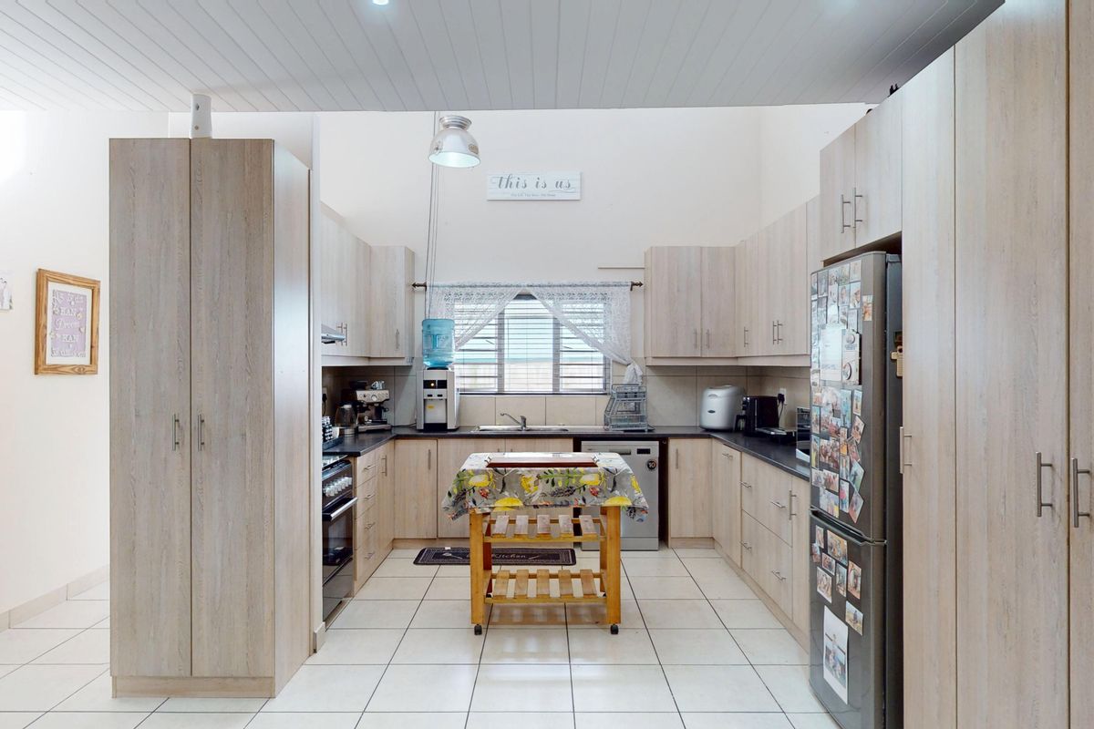 A functional kitchen featuring light wood-toned cabinetry, dark laminate countertops, tiled flooring, and a high-pitched tongue and groove ceiling.