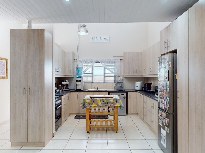 A functional kitchen featuring light wood-toned cabinetry, dark laminate countertops, tiled flooring, and a high-pitched tongue and groove ceiling.