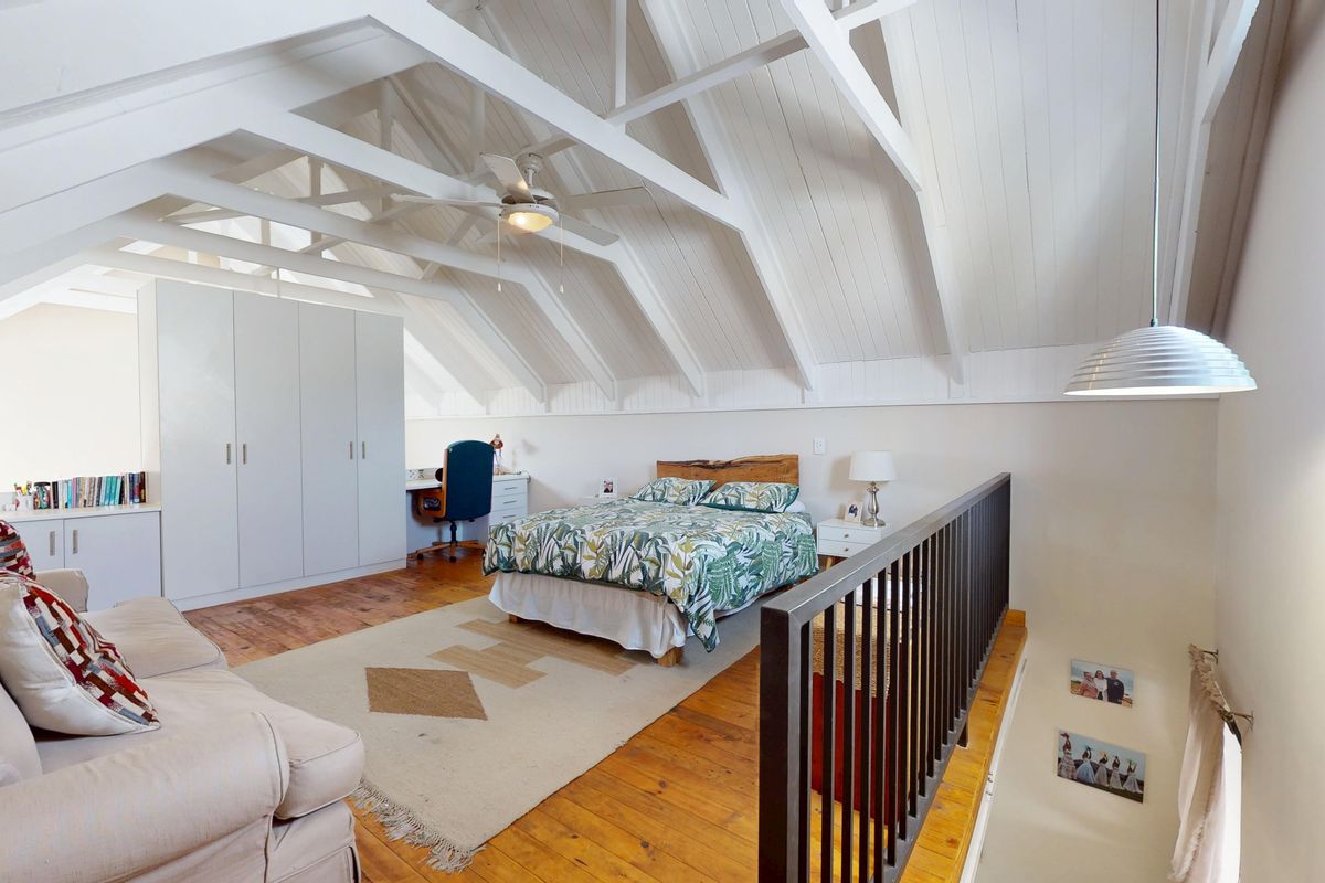Spacious loft-style bedroom featuring vaulted ceilings with exposed timber beams, built-in wardrobes, and warm timber flooring overlooking the lower level.
