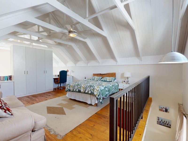 Spacious loft-style bedroom featuring vaulted ceilings with exposed timber beams, built-in wardrobes, and warm timber flooring overlooking the lower level.