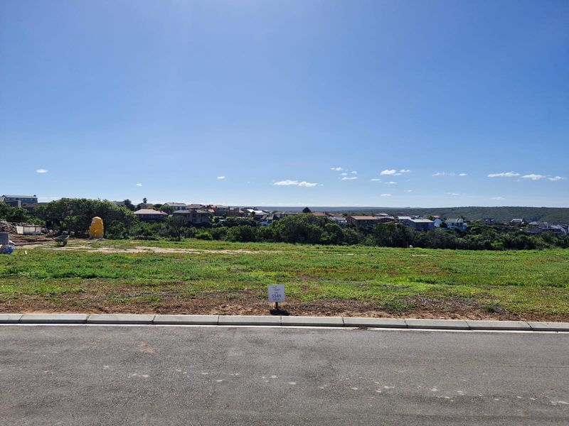A vacant residential plot featuring a clear view of the surrounding neighborhood, accessible via a paved road with established curbing.