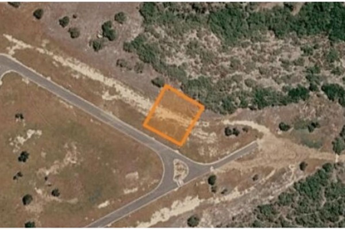 An aerial view of a vacant residential plot highlighted in orange, situated near an access road and natural vegetation.